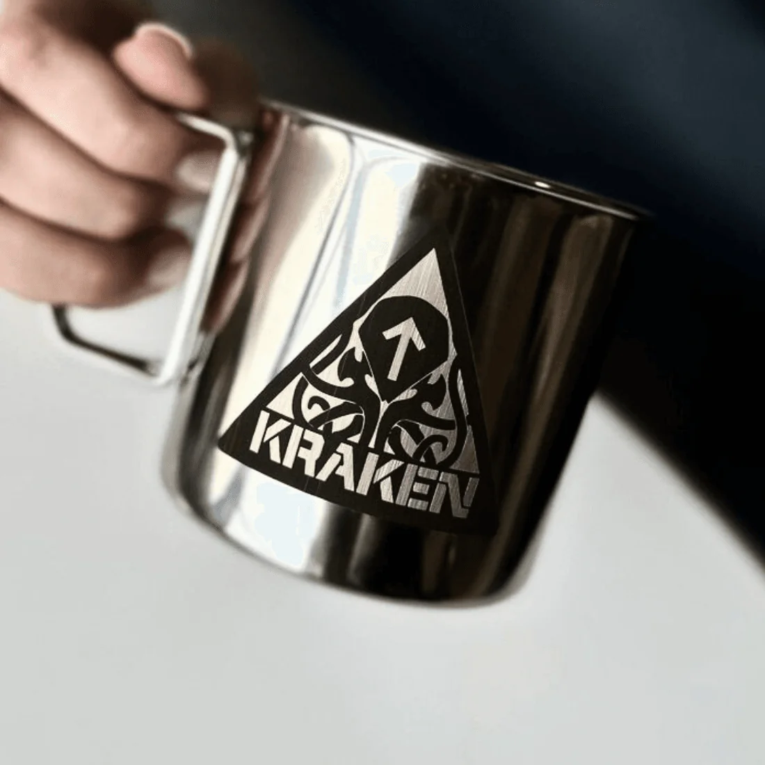 Металева кружка з гравіюванням логотипу Kraken у руці.