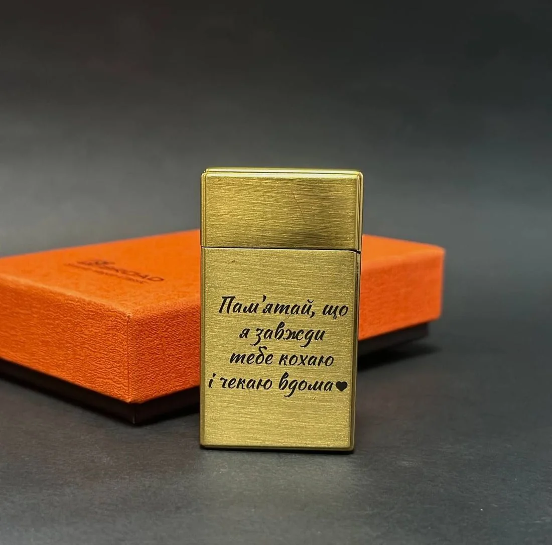 Золота металева запальничка з лазерним гравіюванням на корпусі на зеленому тлі