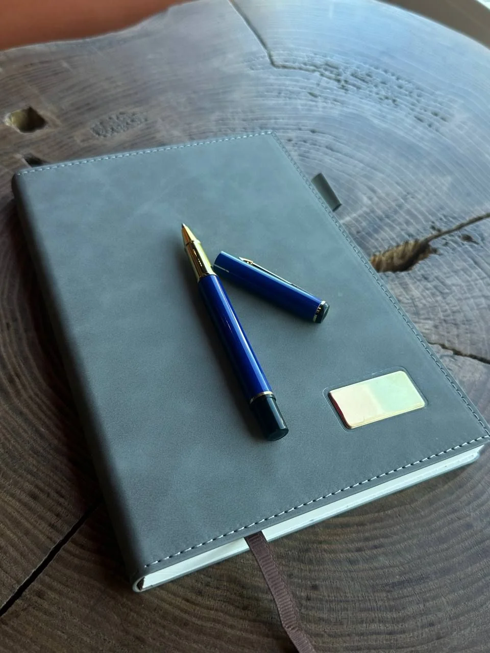 Синя металева ручка з гравіюванням, покладена на блокнот