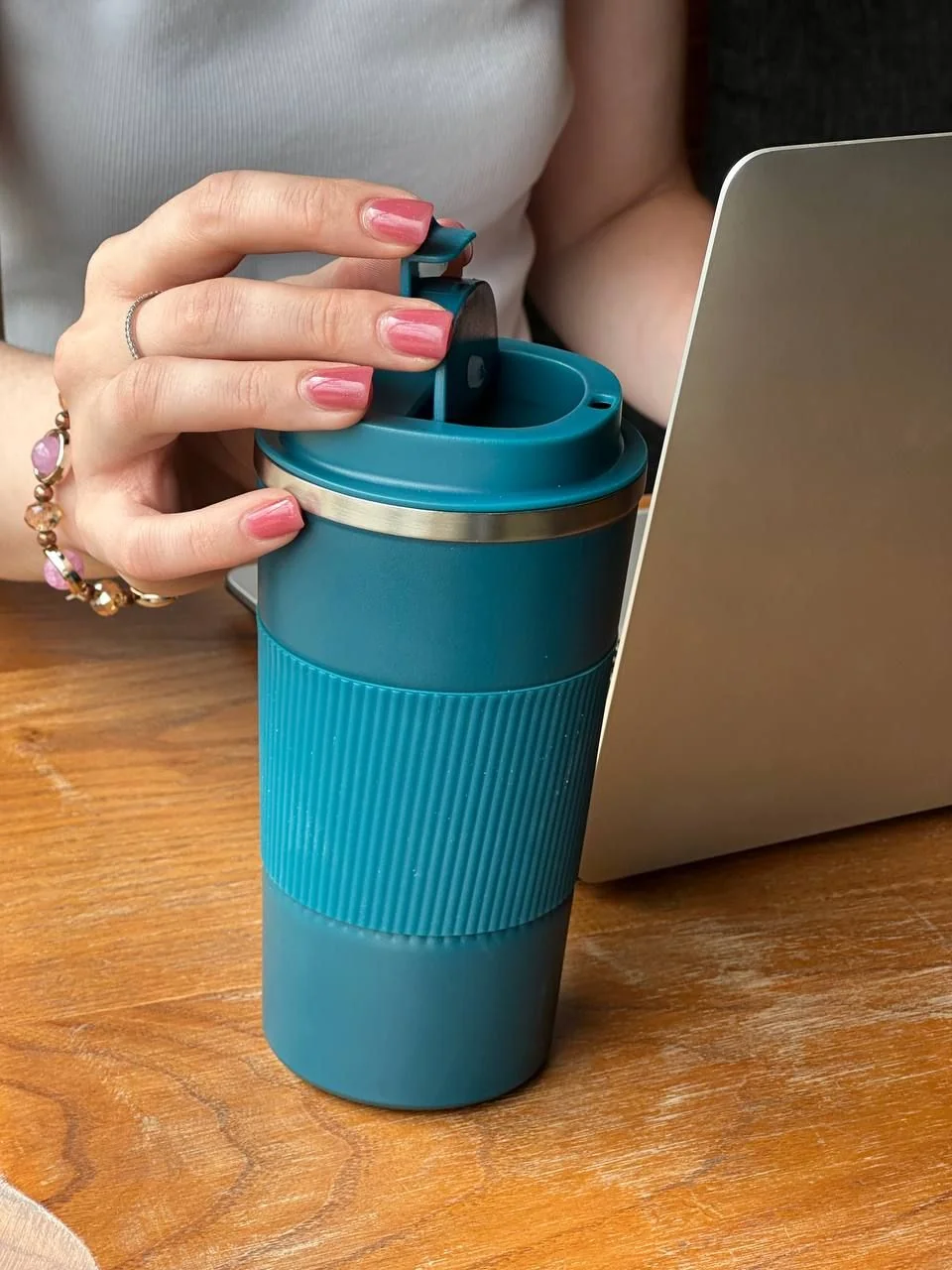 Жінка тримає блакитну термокружку з гравіюванням біля ноутбука