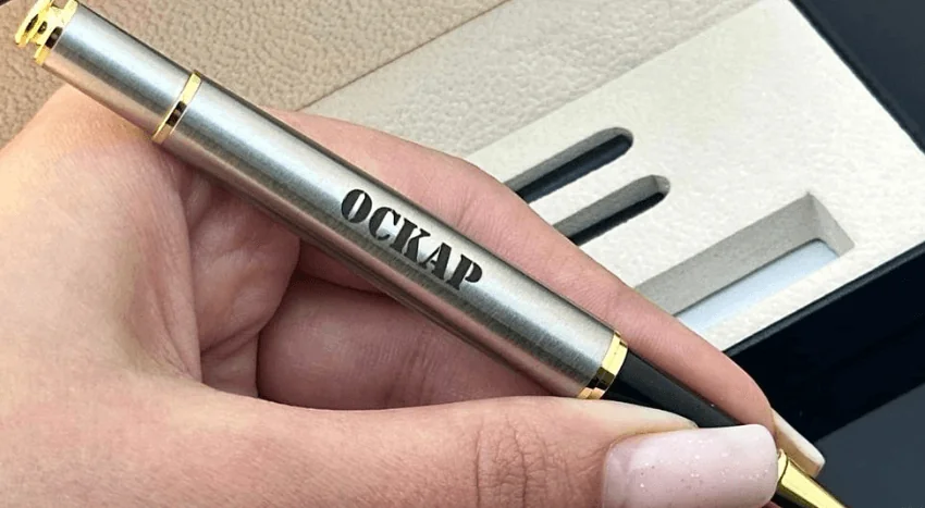 Срібляста ручка з лазерним гравіюванням імені "Оскар" у жіночій руці — ідея подарунка для команди