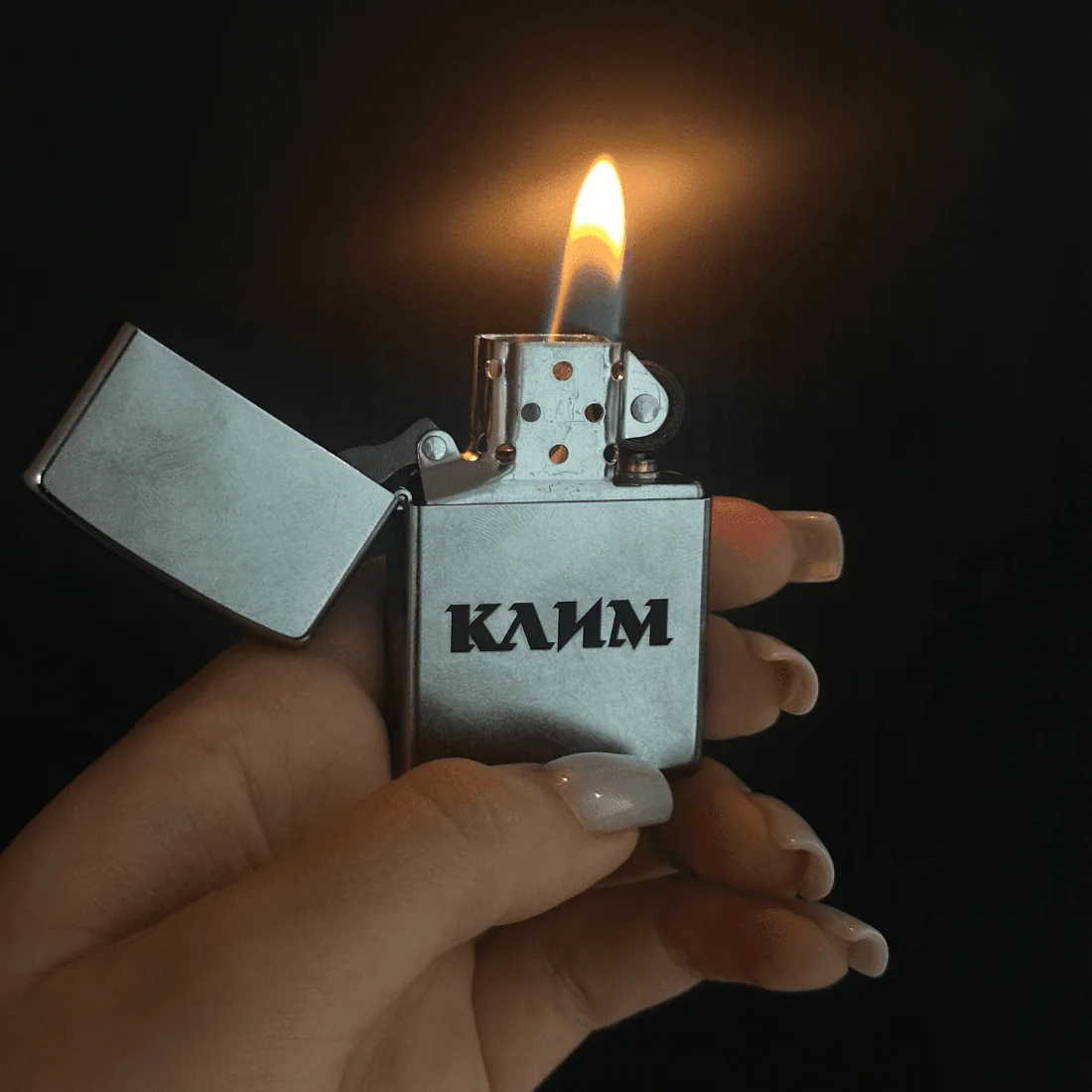 Іменна запальничка Zippo з гравіюванням “КЛИМ” у руці, з відкритим вогнем.